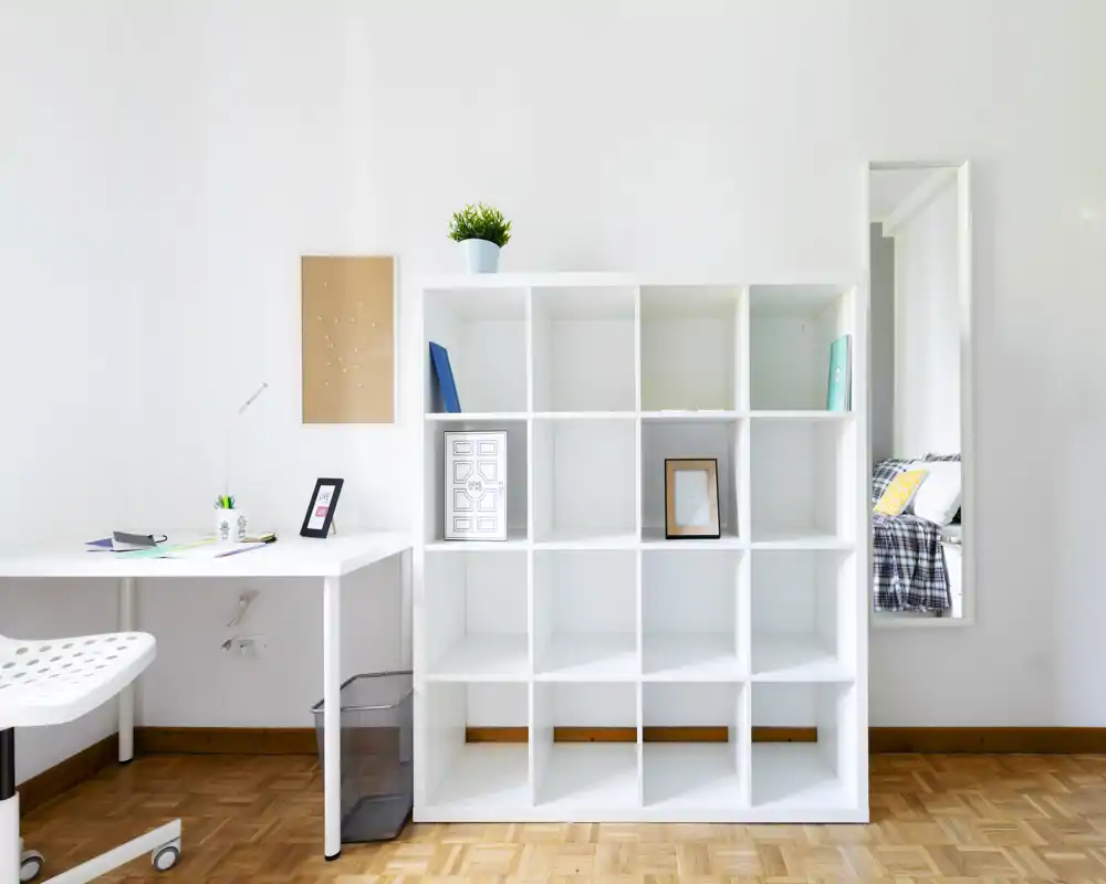 Área de estar luminosa y minimalista con estantería blanca tipo cubo, escritorio y silla — estilo moderno con planta decorativa y marcos.