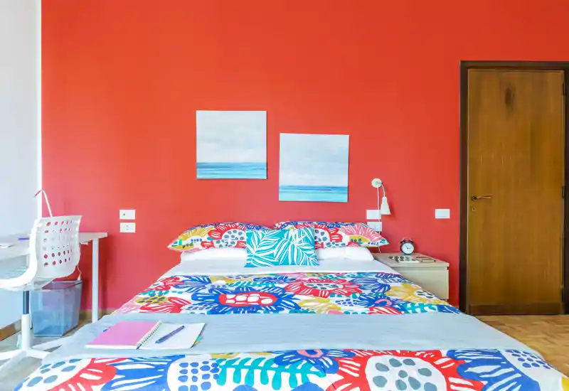 Camera da letto luminosa e colorata con un ampio letto matrimoniale, biancheria a fantasia, comodino e una piccola scrivania — vivace, ben illuminata e curata per un soggiorno accogliente.