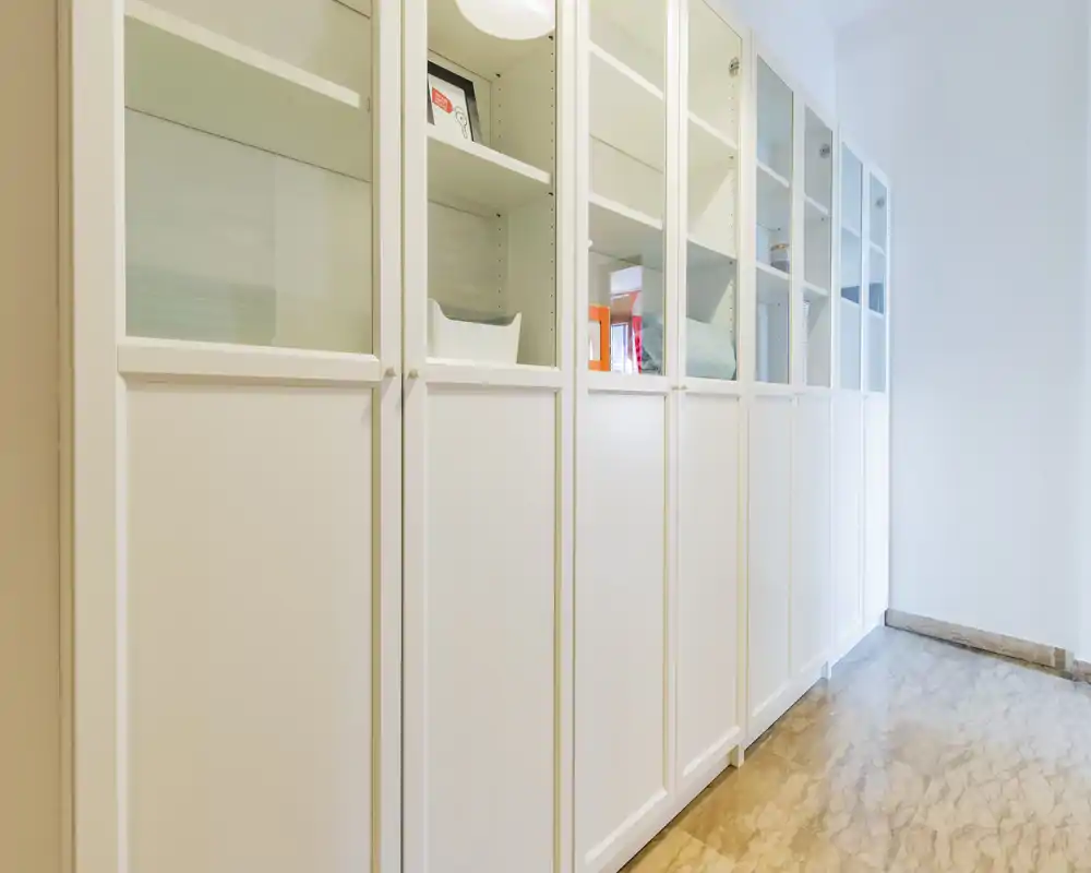A clean, well-lit hallway/storage area with a row of tall white cabinets featuring glass upper doors — ideal for organized storage and a minimal aesthetic.