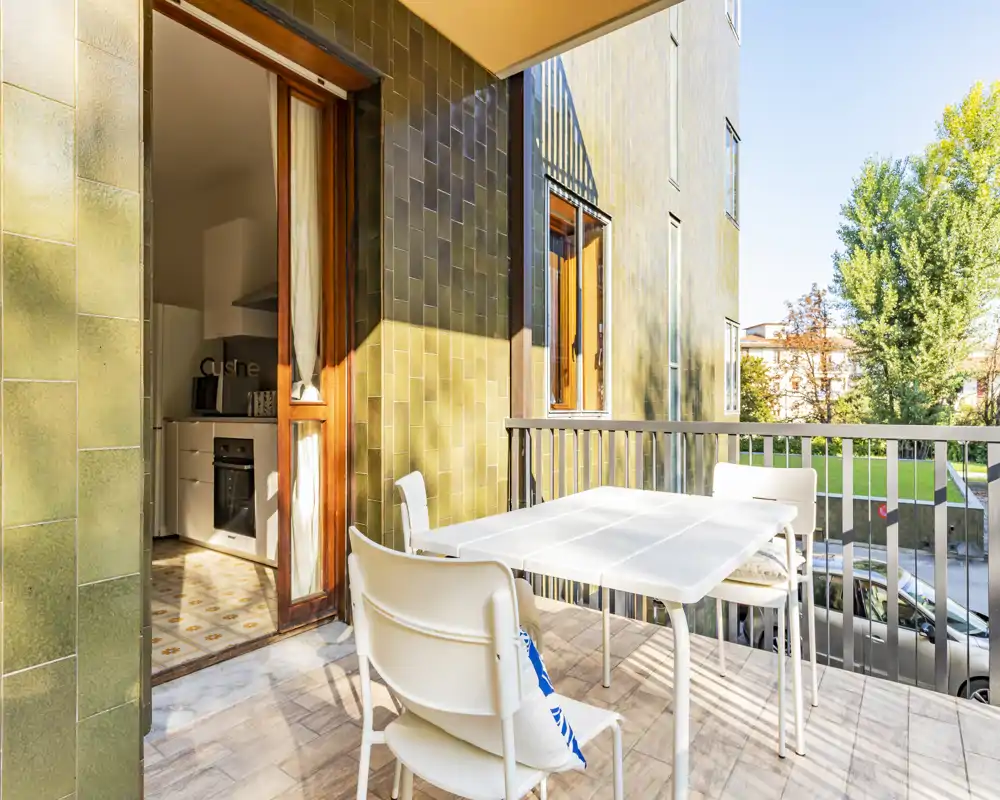 Sunny furnished balcony with a white dining table and chairs, overlooking a green courtyard — ideal for outdoor meals and relaxation.