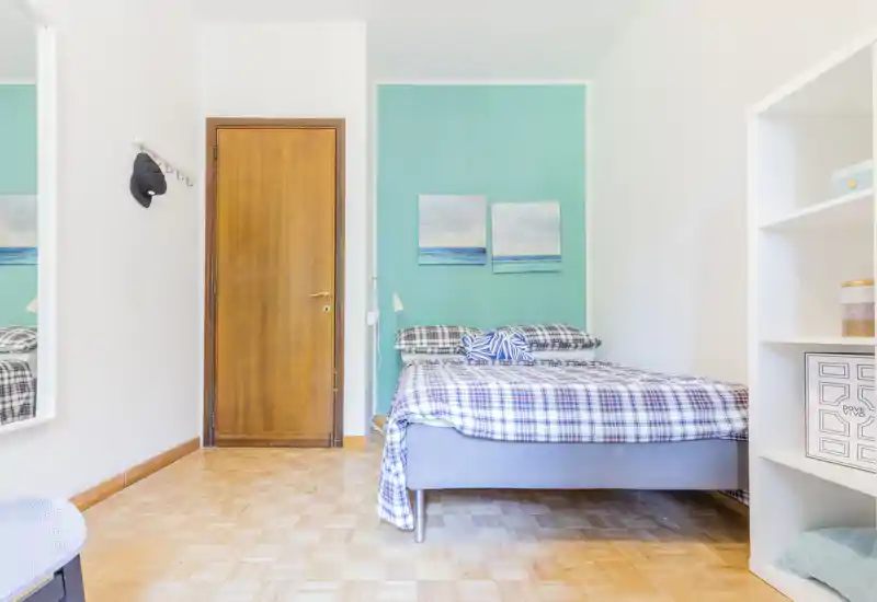 Bright, tidy bedroom with a double bed dressed in plaid linens, coastal artwork and soft natural light—ideal for a cozy stay.