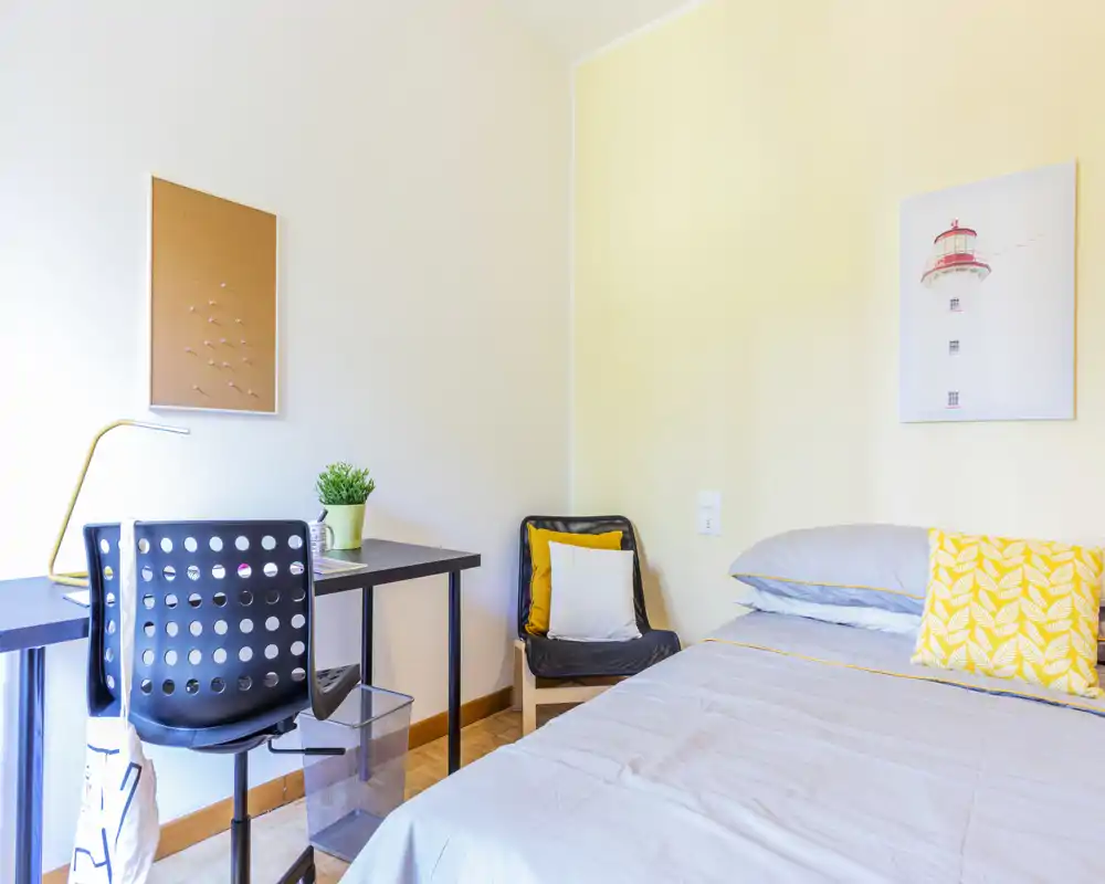 Camera da letto luminosa e ordinata con un letto singolo, una scrivania compatta e una poltroncina accogliente — perfetta per studenti o soggiorni brevi.