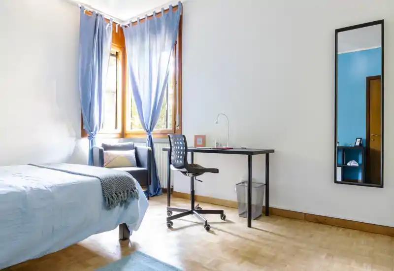 Bright, well-staged bedroom with a double bed, a study desk and a cozy armchair by the window letting in abundant natural light.