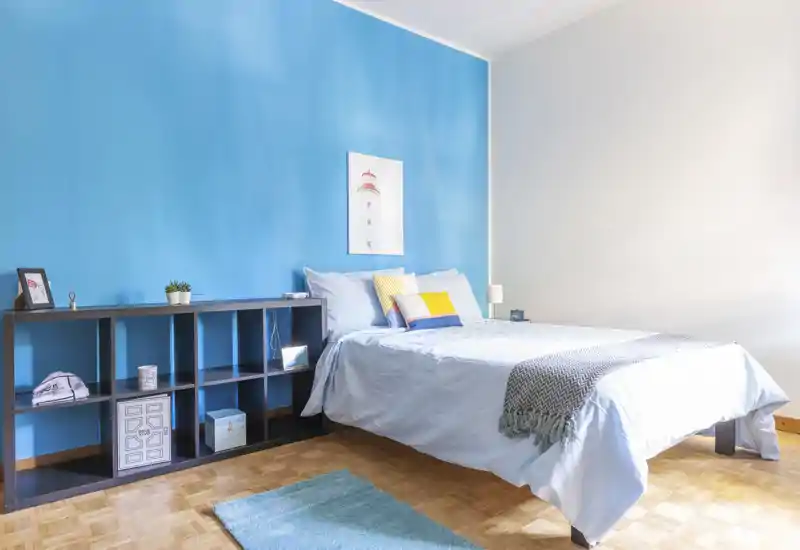 Bright, modern bedroom with a neatly made double bed against a vivid blue accent wall, decorative pillows and a cozy throw — ideal for rental photos highlighting comfort and style.