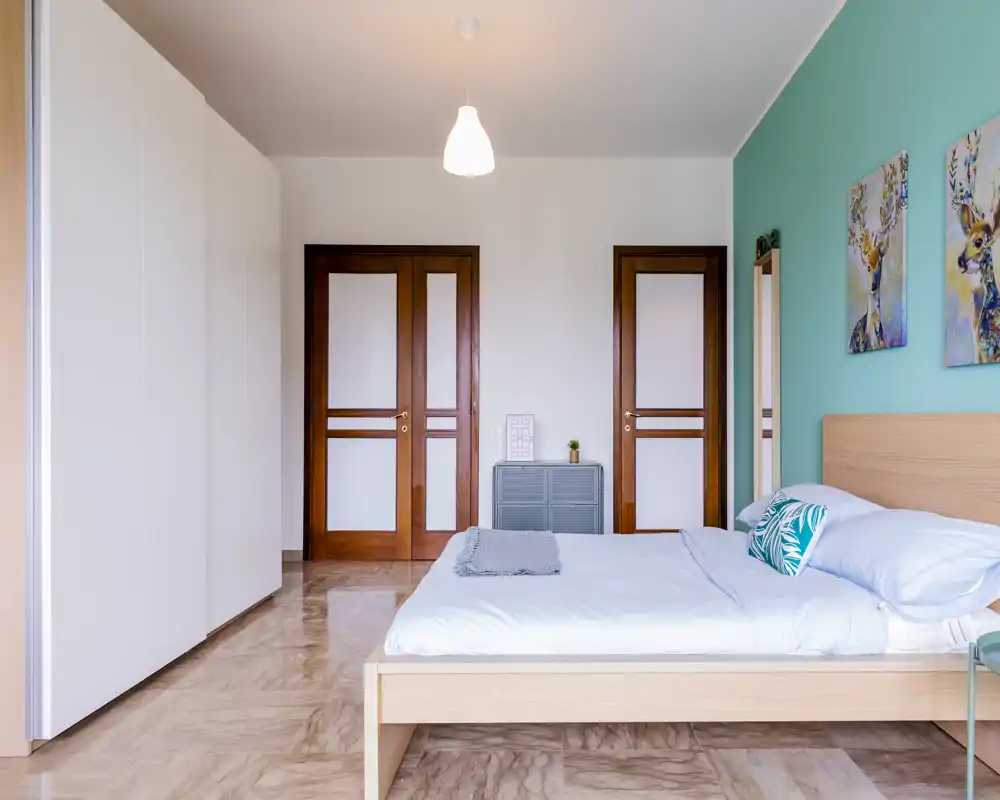 Spacious, bright bedroom with a wooden platform bed, teal accent wall and modern wardrobe — tidy, comfortable and well-lit for rental photos.