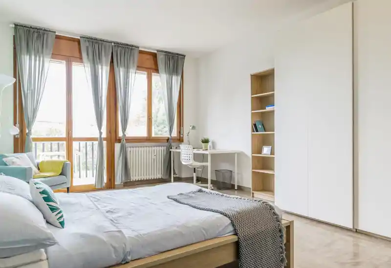 Bright, modern bedroom with a double bed, large windows and a small workspace; neutral tones and soft textiles create a welcoming, airy atmosphere.