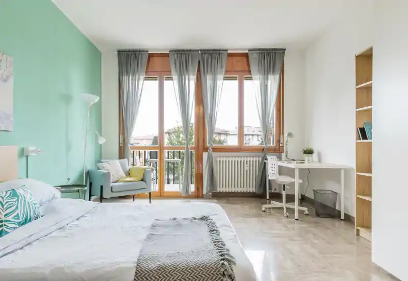 Bright, modern bedroom with a large double bed, soft textiles, an armchair and a desk by spacious windows that let in abundant natural light.