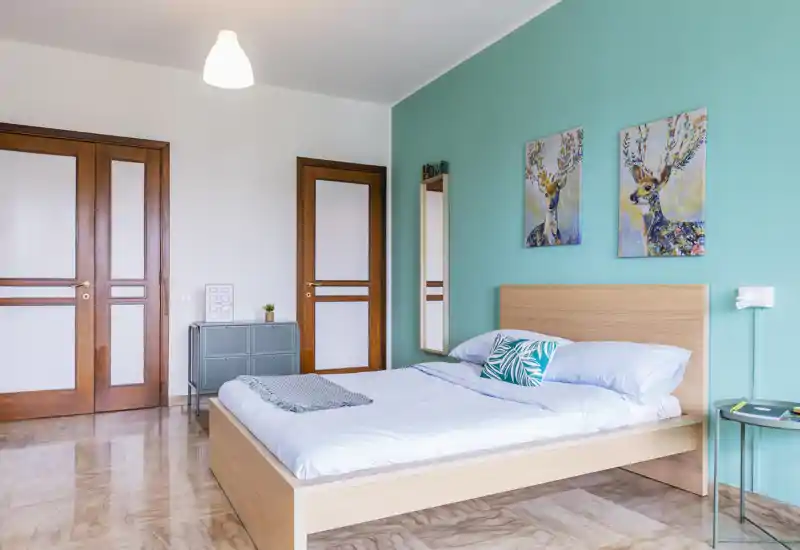 Bright, modern bedroom with a wooden platform bed against a teal accent wall, decorative cushions and matching wall art — ideal for rental listings highlighting style and comfort.