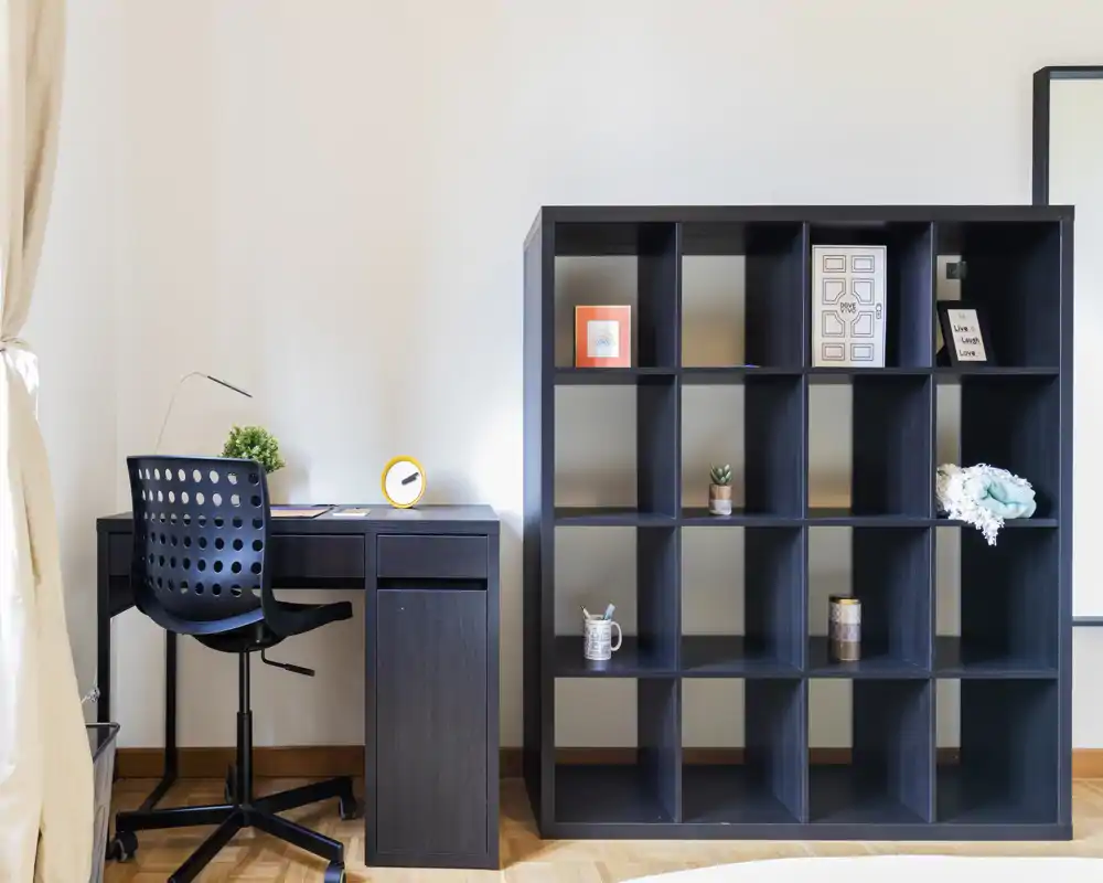 Bright, minimal study corner with a dark wood desk and shelving unit; neat decorative accents and a modern chair create a clean, functional workspace.
