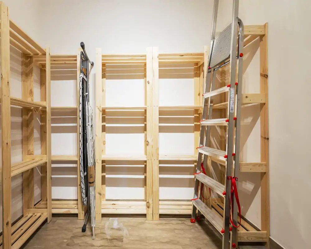 Utility / storage space with unfinished pine shelving, a folding drying rack and a step ladder on a concrete floor — a tidy, empty storeroom suitable for organization or moving-in preparation.