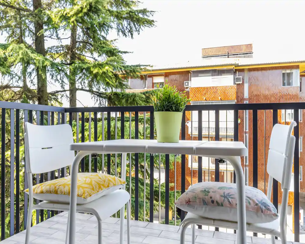 Balcón privado soleado con mesa pequeña, dos sillas y cojines decorativos — ideal para el café de la mañana o para relajarse al aire libre.