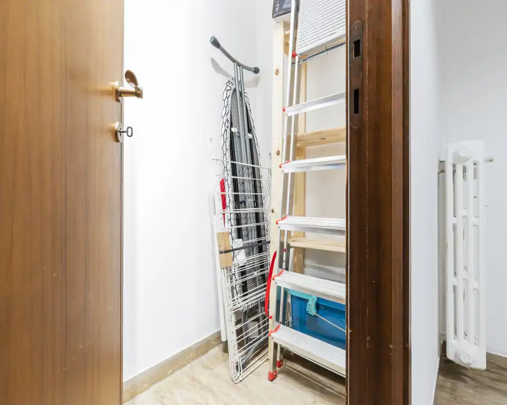 Piccolo ripostiglio/guardaroba di servizio con scala pieghevole, asse da stiro e stendibiancheria: uno spazio utile per riporre attrezzi e accessori.