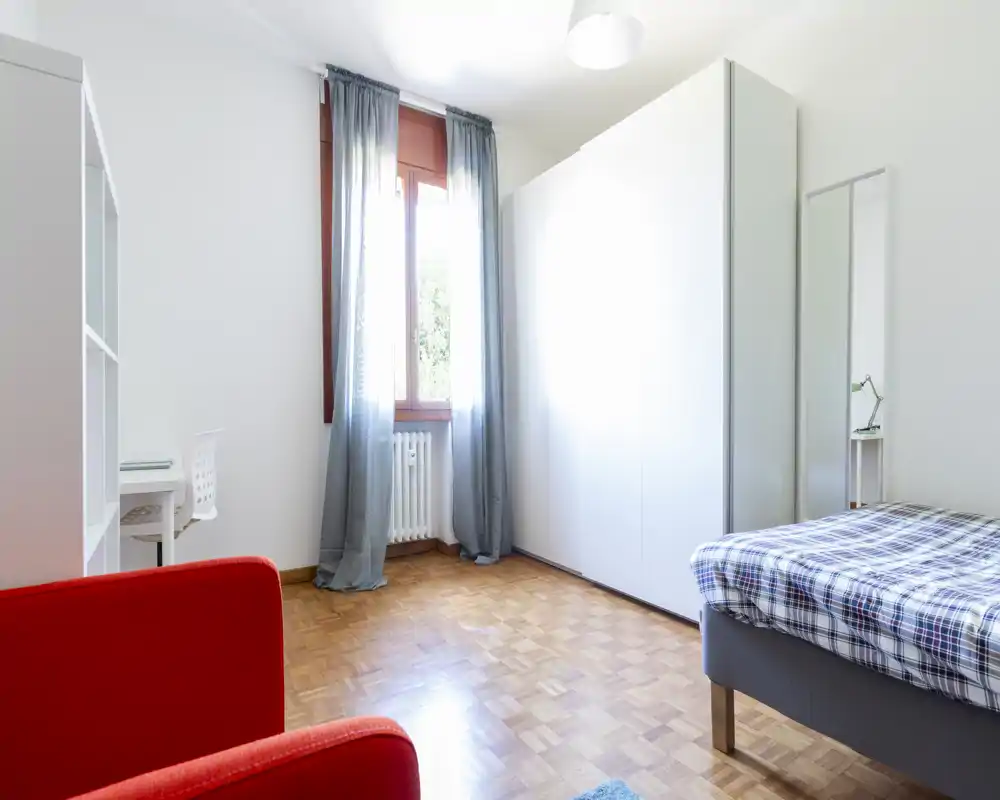 Dormitorio luminoso y moderno con cama individual bien hecha, amplio armario y luz natural por la ventana. Estilo minimalista y suelo de parquet que crean un ambiente fresco y acogedor, perfecto para anuncios.