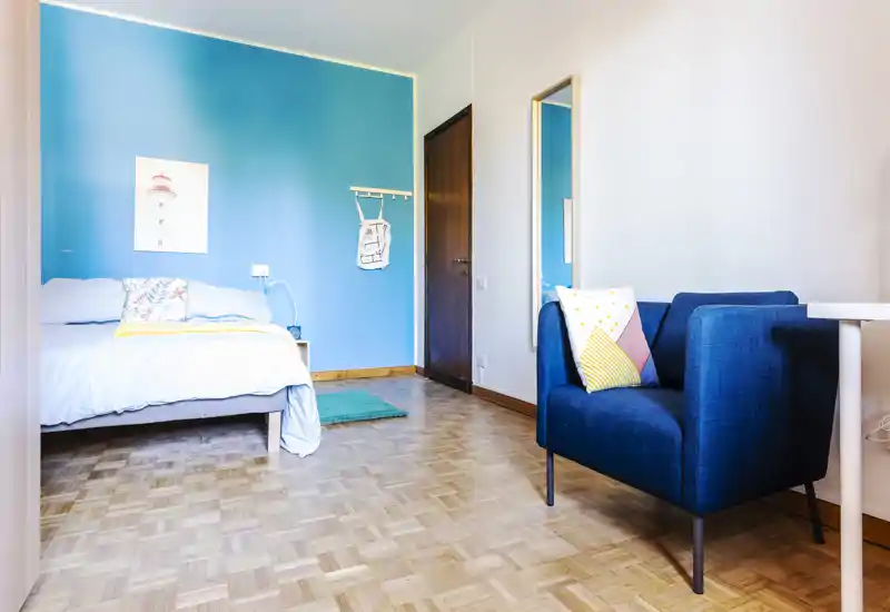 Bright, cozy bedroom with a blue accent wall, double bed with decorative pillows and a comfortable armchair — ideal for a relaxing stay.