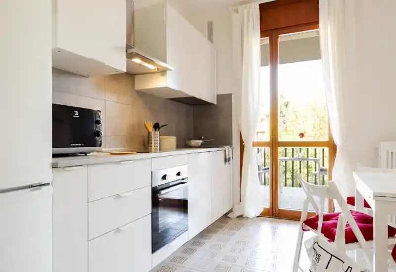 Bright modern kitchen with white cabinets, built-in oven, and a glass door opening to a balcony that brings abundant natural light.