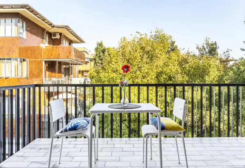 Sunny private balcony with a small table and two chairs, tiled floor and leafy view — ideal for morning coffee.