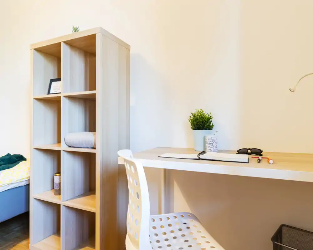 Bright, minimal bedroom corner with a desk and shelving: a compact workspace next to a partially visible bed, plant accents and clean, modern lines.
