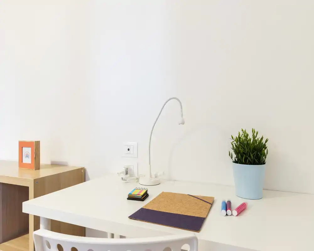 Bright, minimal desk corner with a small lamp, potted plant and stationery — a tidy workspace suitable for study or home office.