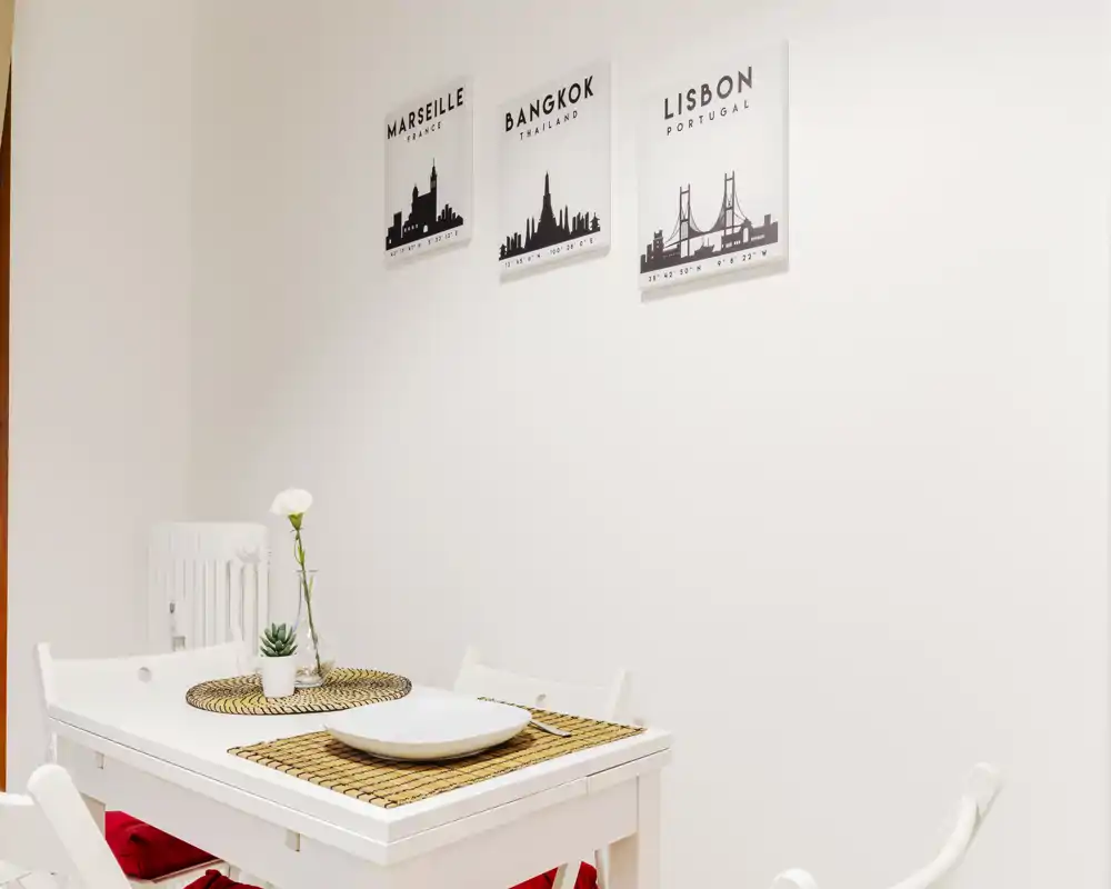 Small, bright dining area with a white table set for two, woven placemats and minimalist wall art — ideal for cozy meals.