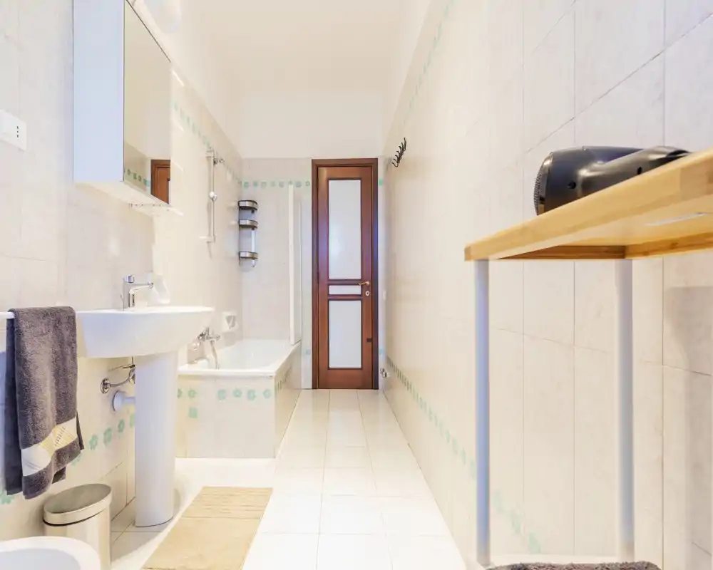 Bright, well-lit bathroom with a bathtub, pedestal sink, mirror cabinet and tiled walls; neutral decor ideal for rental listings.