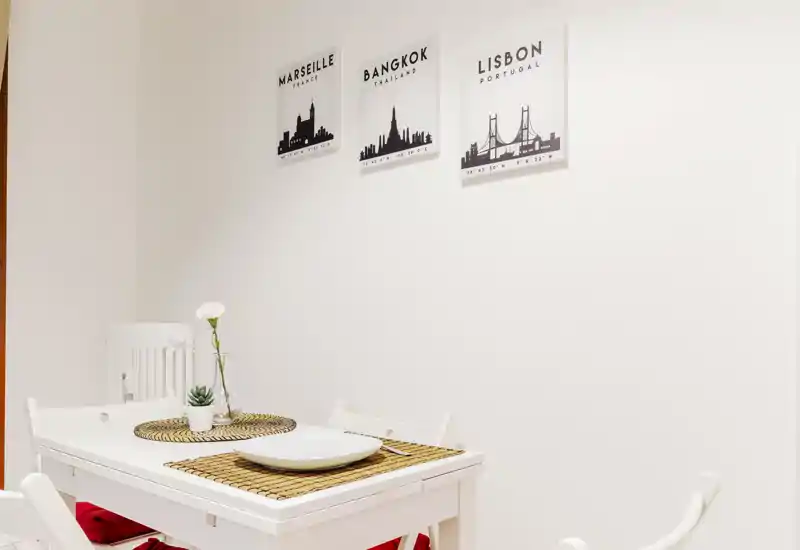 Small, bright dining area with a white table set for two, woven placemats and minimalist wall art — ideal for cozy meals.