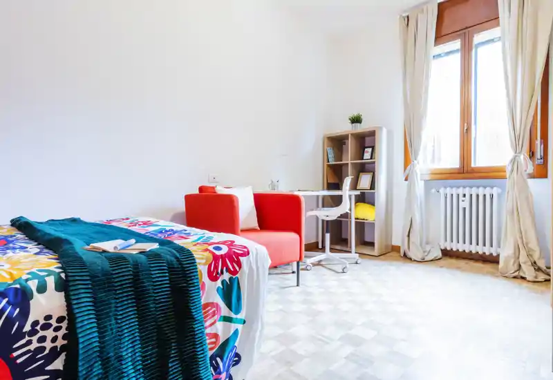 Bright, well-styled bedroom with a colorful bedspread, cozy throw and a small workspace by the window — perfect for both relaxation and study.