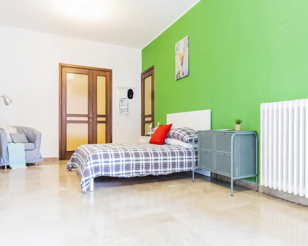 Bright, modern bedroom with a double bed dressed in checked linens, a green feature wall and a small bedside console — clean, airy and well-lit.
