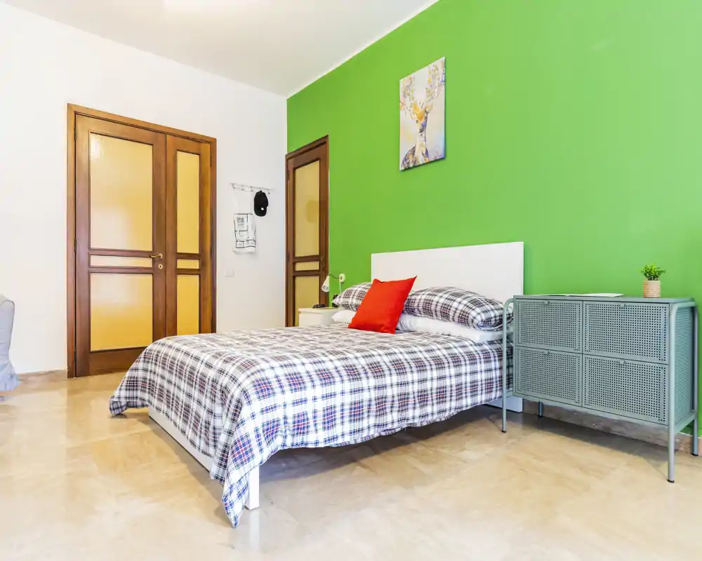 Bright, modern bedroom with a queen bed dressed in checkered linens, a vivid green accent wall and simple bedside storage—ideal for a comfortable stay.