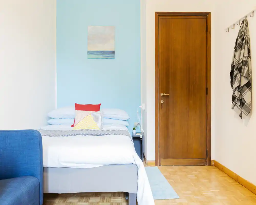 Chambre lumineuse et soignée avec un lit double devant un mur bleu doux, coussins colorés et table de chevet — idéale pour des annonces locatives mettant en avant confort et style.