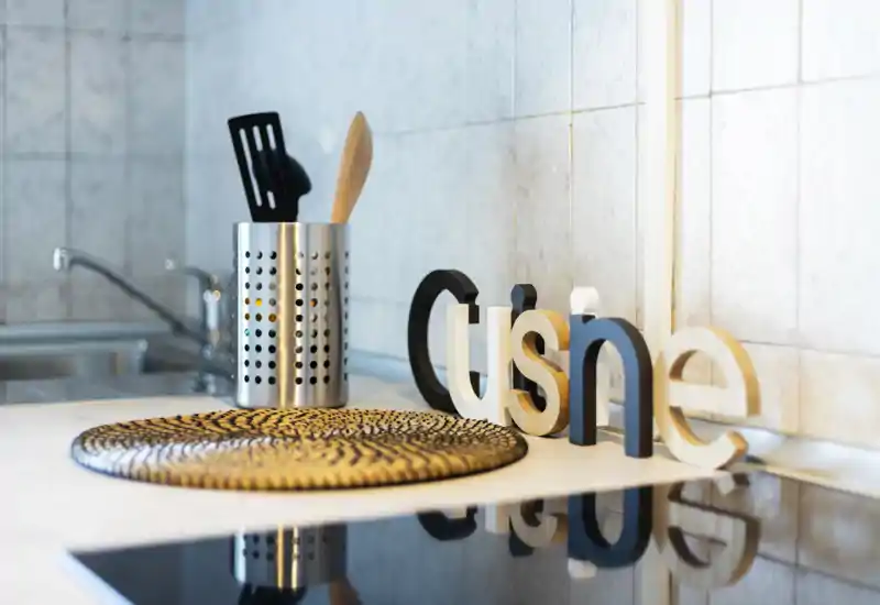 Close-up of a modern kitchen countertop with utensil holder, decorative "cuisine" letters and an induction hob — bright, styled shot ideal for a listing highlighting kitchen details.
