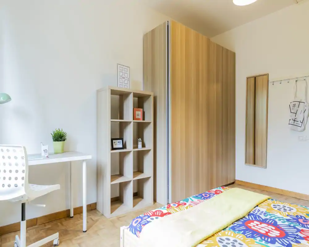Bright, modern bedroom with colorful bedding, a wardrobe, shelving unit and a small desk — ideal for comfortable short or long stays.