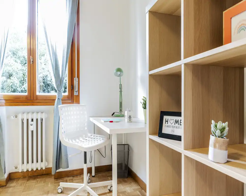 Bright, compact home office corner with a white desk, ergonomic chair and wooden shelving — ideal for remote work or study.