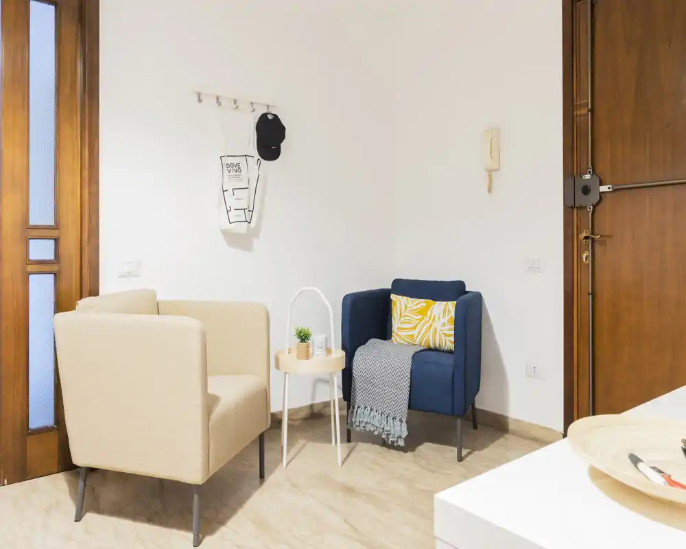 A compact, well-lit living corner with two armchairs, a small side table and tasteful cushions and throws, ideal for relaxing or reading.