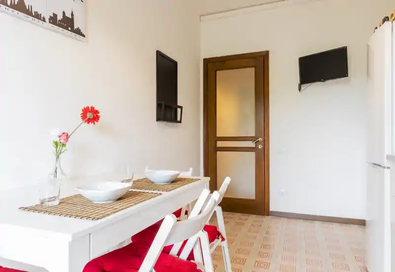 Bright, compact dining area with a white table set for two, woven placemats and red-cushioned folding chairs — a neat, modern spot for casual meals.