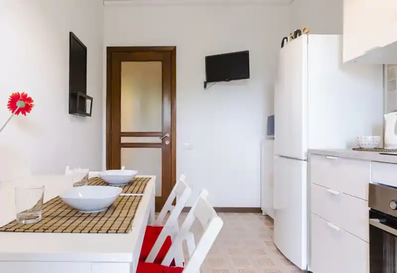 Compact bright kitchen with a small dining table set for two, white cabinetry, fridge and tasteful placemats that create a clean, welcoming space.
