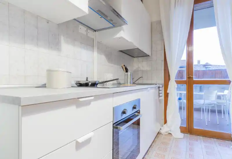 Bright modern kitchen with white cabinets, built-in oven and a glass door opening to a small balcony; clean countertops and natural light create an inviting cooking area.