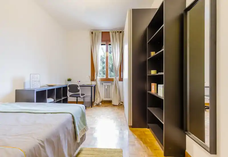Bright, well-styled bedroom with a comfortable bed, desk by the window and built-in shelving; warm wooden floors and soft textiles create a welcoming atmosphere.