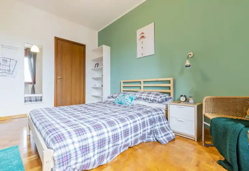 Bright, freshly styled bedroom with a double bed, patterned bedding and green accent wall. Natural light, bedside table and cozy seating create a welcoming atmosphere ideal for listings.