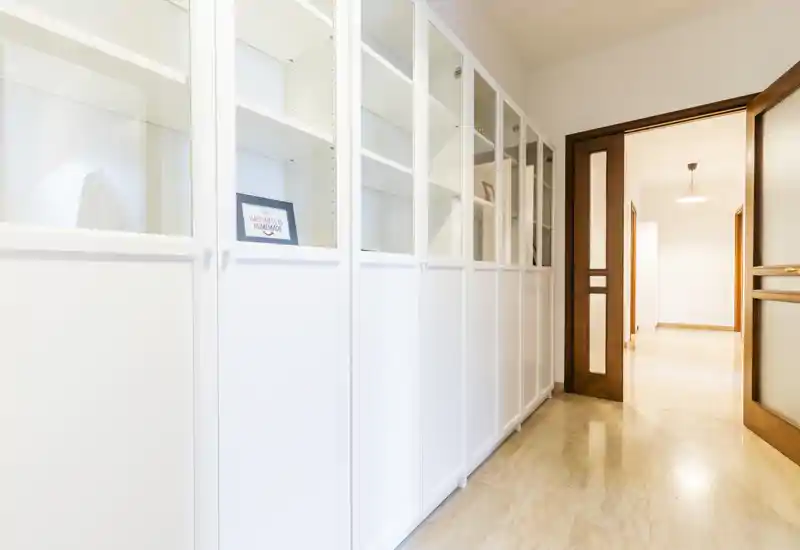Bright, clean entrance corridor with built-in white storage cabinets and a warm wooden doorway leading into the home.
