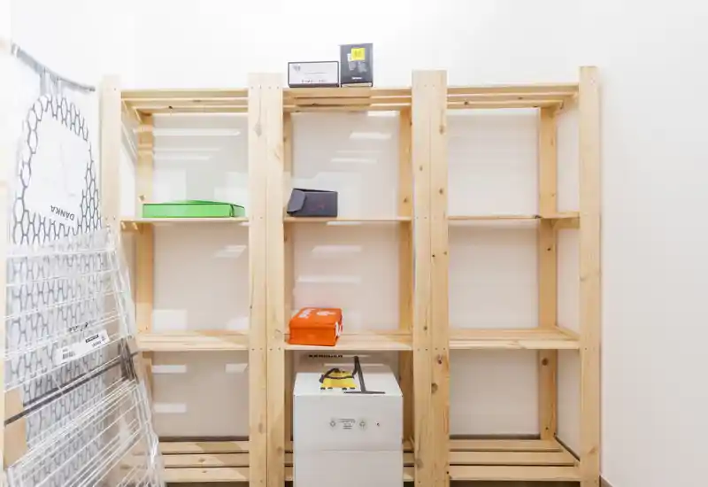 Small storage or entrance area with wooden shelving units and a few packed items; bright, utilitarian space suitable for storing household goods.