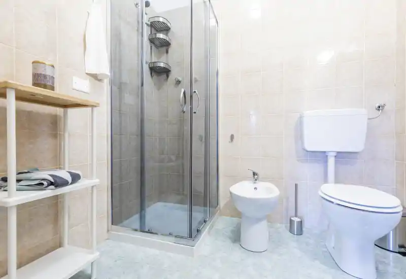 Bright, clean bathroom with a glass-enclosed shower, bidet and toilet on tiled walls and floor — practical and well maintained.