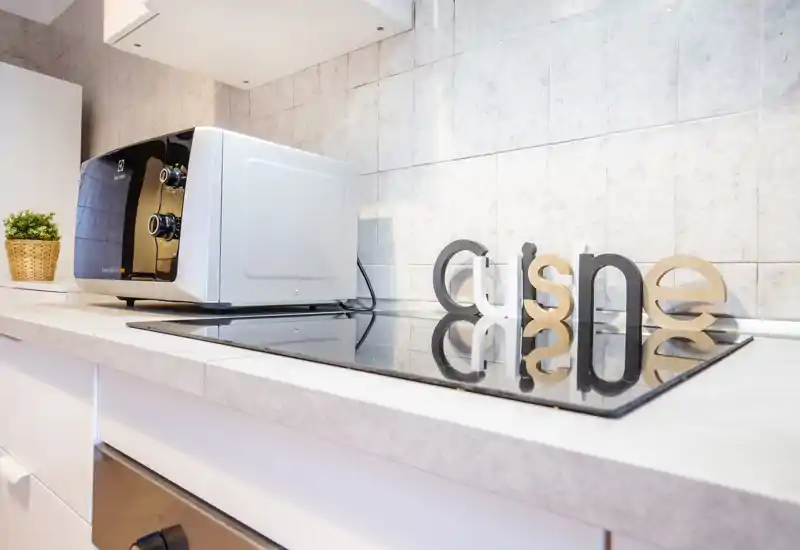 Bright, modern kitchen countertop with a built-in glass hob, a compact toaster/oven and decorative accents — neat and well lit for a short-stay listing.