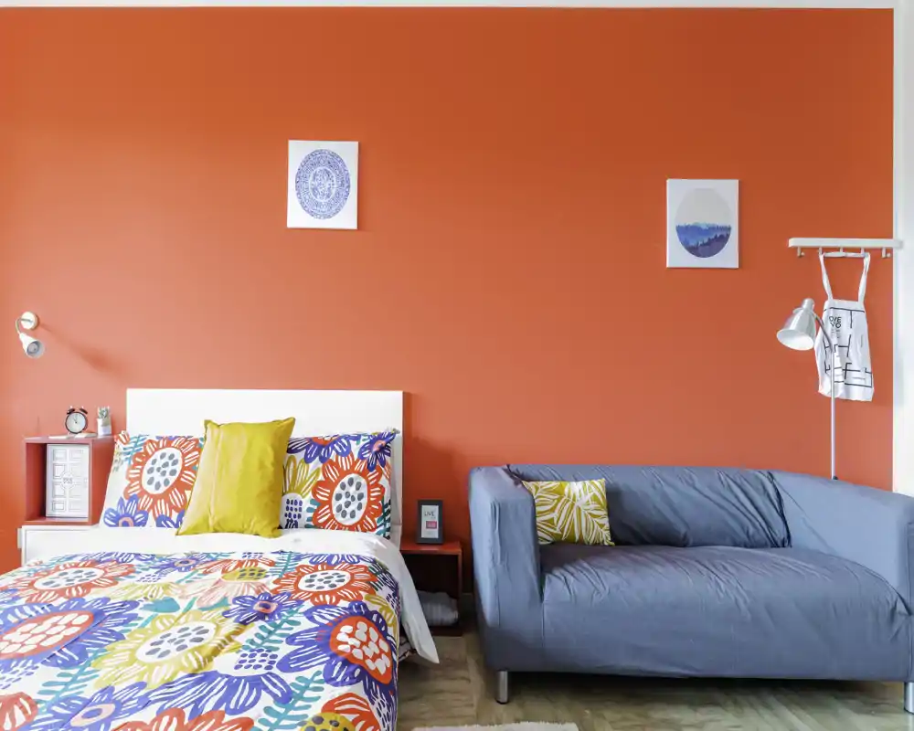 Camera da letto luminosa e colorata con copriletto fantasia, cuscino vivace e un piccolo divano accanto al letto — ariosa, ben illuminata e ideale per foto di annunci.