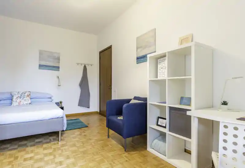 Bright, modern bedroom with a neatly made double bed, a cozy blue armchair and a white shelving unit — ideal for a stylish rental listing.