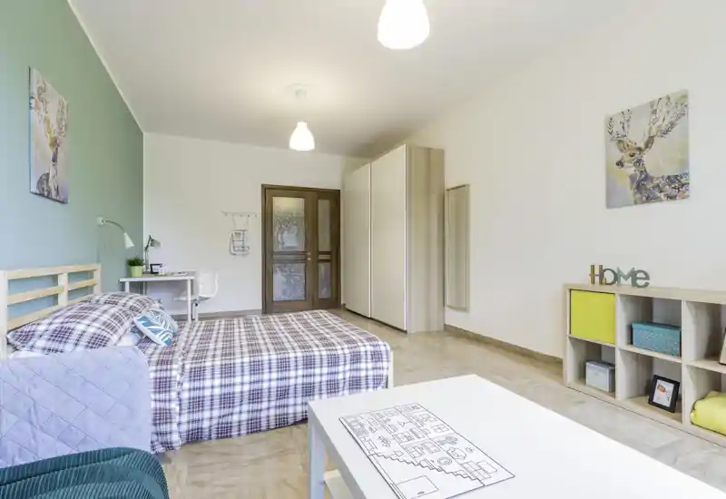 Camera luminosa e ben arredata con letto matrimoniale in copriletto a quadri, scrivania vicino al muro e armadio a muro — arredo moderno e accogliente ideale per affitti brevi.