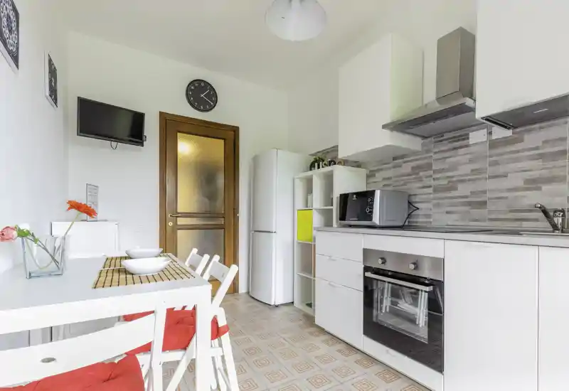Bright, modern kitchen with integrated oven, microwave and fridge. A small dining area with white table and chairs, decorative flowers and cushions creates a welcoming, functional space.