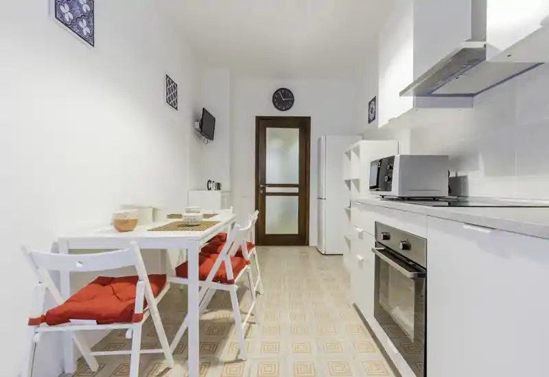 Bright, modern kitchen with white cabinets, built-in oven, microwave and a small dining table with red-cushioned chairs — ideal for compact apartment listings.