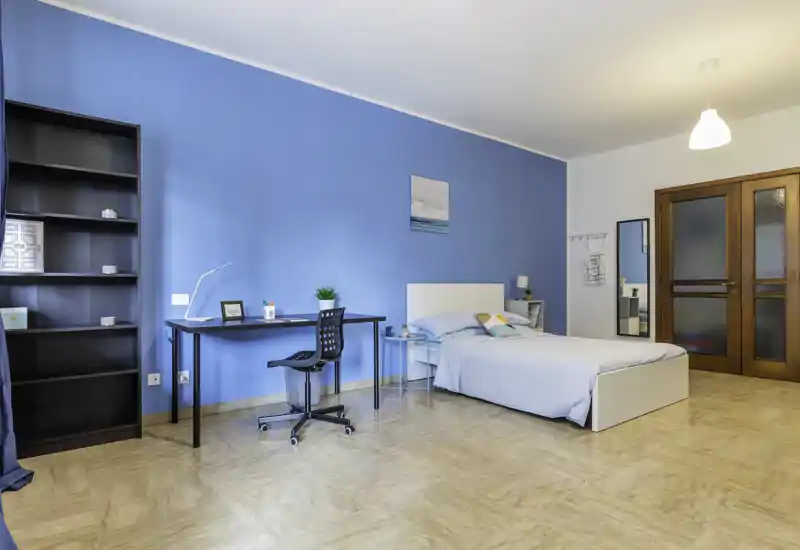 Chambre spacieuse et lumineuse avec mur bleu, lit simple, table de chevet et bureau bien rangé — idéale pour étudiant ou professionnel.