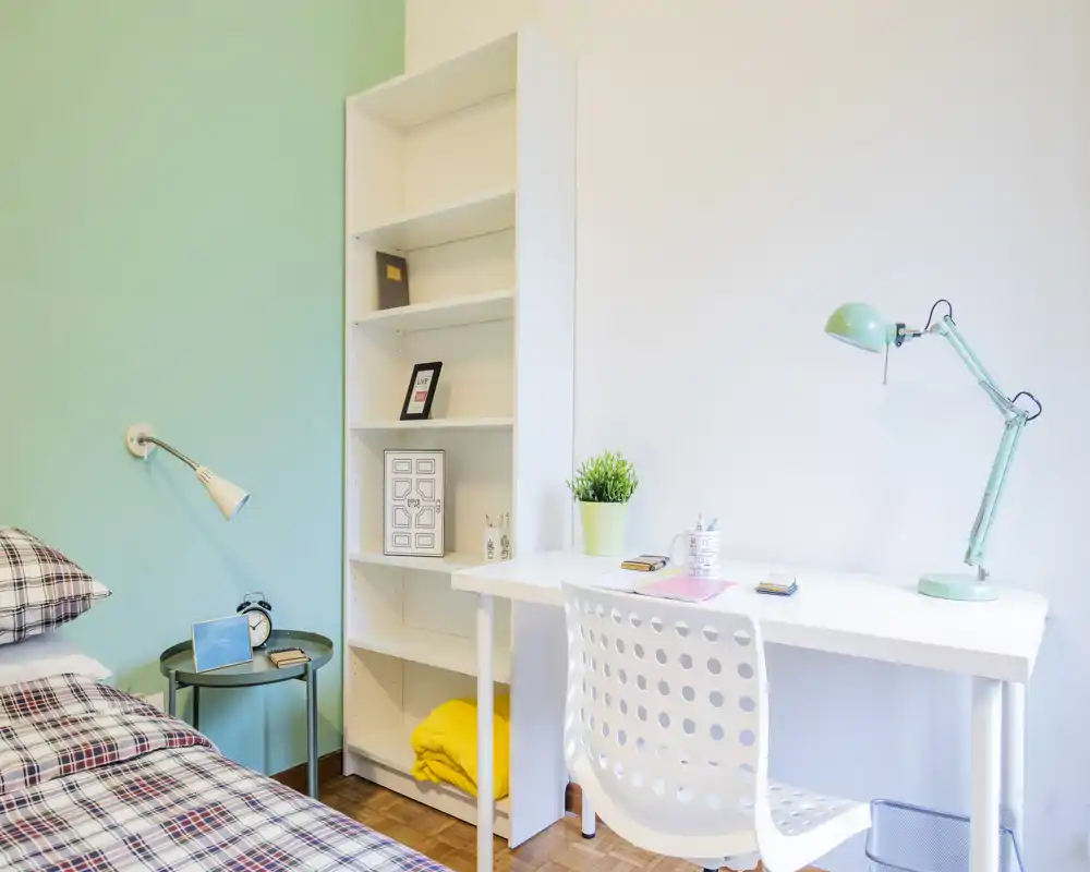 Rincón de dormitorio luminoso y moderno con cama a cuadros, mesita y escritorio blanco con lámpara verde menta: líneas limpias, tonos pastel y textiles acogedores crean un ambiente fresco y agradable.