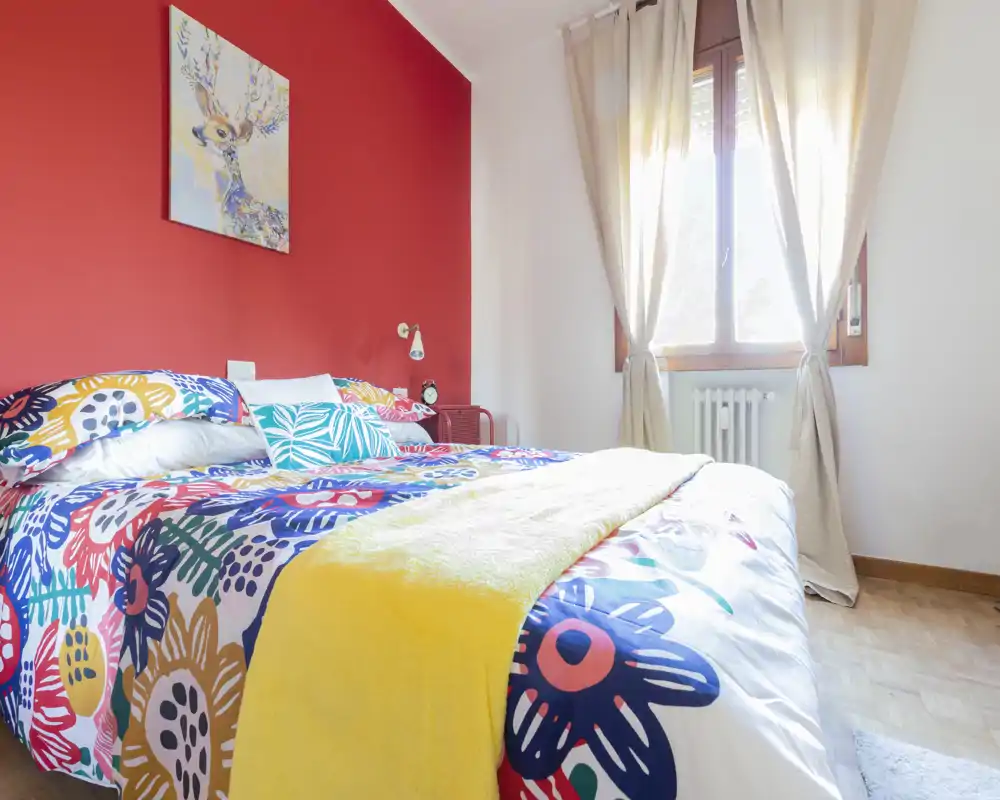 Dormitorio luminoso y colorido con cama grande, edredón de estampado y luz natural desde la ventana — espacio acogedor y bien decorado, perfecto para el anuncio.